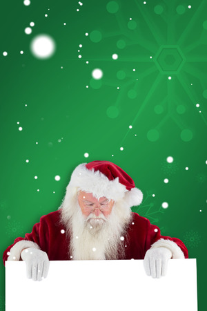 Santa holds a sign and looks down against green snowflake backgroundの写真素材