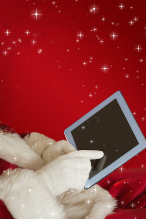 Santa using tablet on the armchair against red snowflake backgroundの写真素材