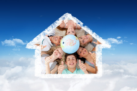 Teenagers on the floor with a terrestrial globe in the center and with thumbs up against bright blue sky over cloudsの写真素材