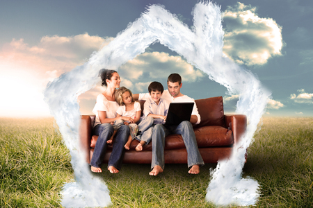 Happy family using the laptop in a field against house outline in cloudsの写真素材