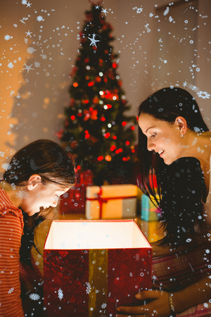 Festive mother and daughter opening a glowing christmas gift against snow fallingの写真素材