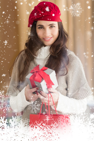 Smiling brunette holding gift and shopping bags against snow fallingの写真素材