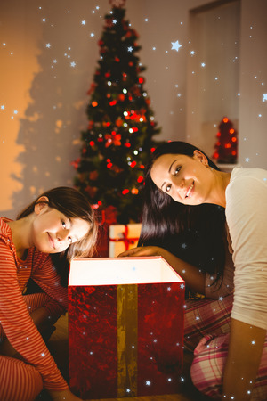 Festive mother and daughter opening a glowing christmas gift against snow fallingの写真素材