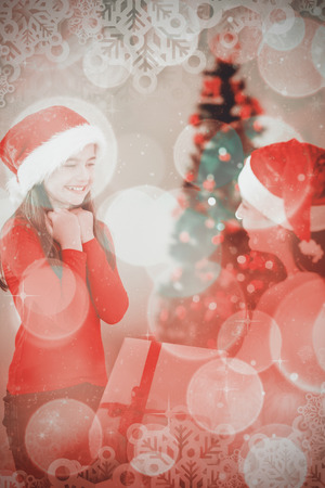 Mother giving her daughter a christmas present  against twinkling red and orange lightsの写真素材