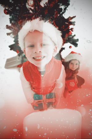 Festive little siblings smiling at camera holding gifts against candle burning against festive backgroundの写真素材