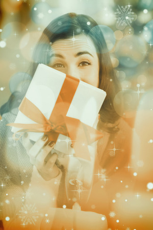 Brunette showing gift on the couch at christmas against candle burning against festive backgroundの写真素材