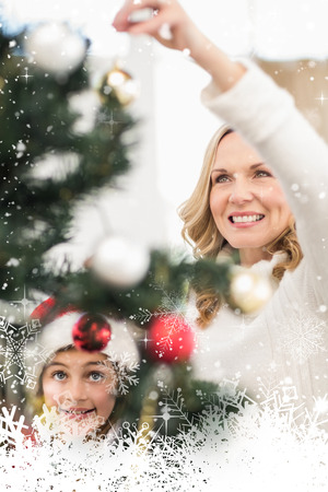 Festive mother and daughter decorating christmas tree against snow fallingの写真素材