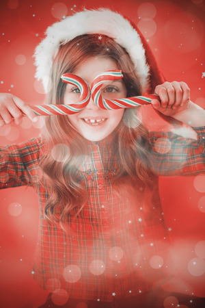 Happy little girl in santa hat holding candy canes against digitally generated twinkling light designの写真素材