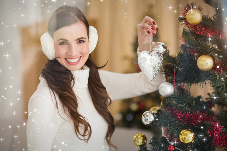 Smiling brunette holding heart near a christmas tree against twinkling starsの写真素材