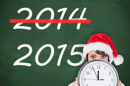 Festive brunette holding a clock against green chalkboard