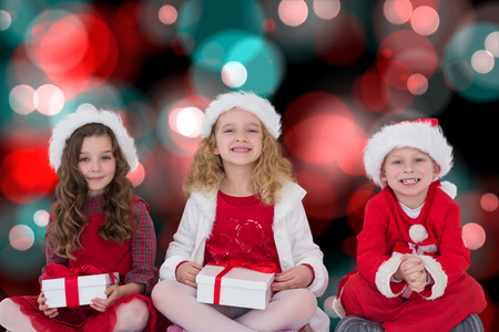 Festive little siblings smiling at camera holding gifts against digitally generated twinkling light designの写真素材