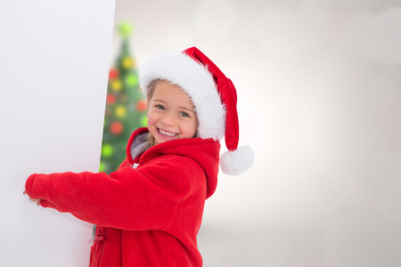 Festive little girl showing poster against blurry christmas tree in roomの写真素材