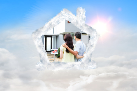 Newlyweds with their new house against blue sky with white cloudsの写真素材