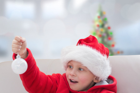 Cute boy holding bauble against blurry christmas tree in roomの写真素材