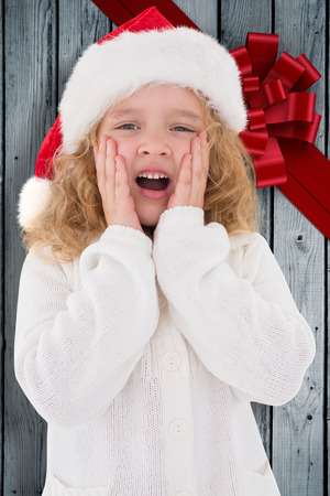 Festive little girl with hands on face against wood with festive bowの写真素材