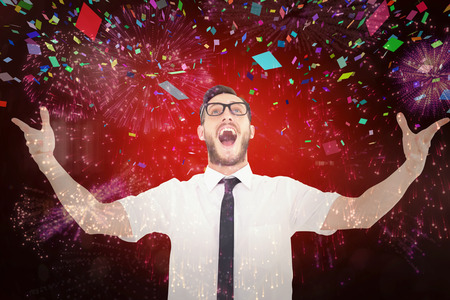 Geeky young businessman with arms out against colourful fireworks exploding on black backgroundの写真素材