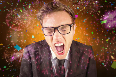 Young angry businessman shouting at camera against colourful fireworks exploding on black background