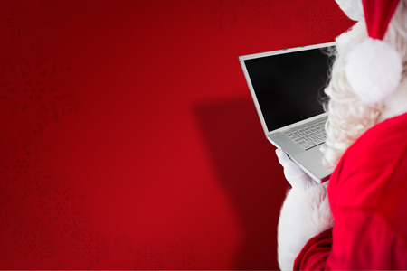 Santa claus using his laptop  against red snowflake backgroundの写真素材