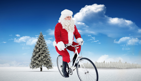 Cheerful father christmas cycling  against fir tree in snowy landscapeの写真素材