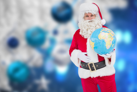 Happy santa claus holding a globe against christmas decorations hanging from branchの写真素材