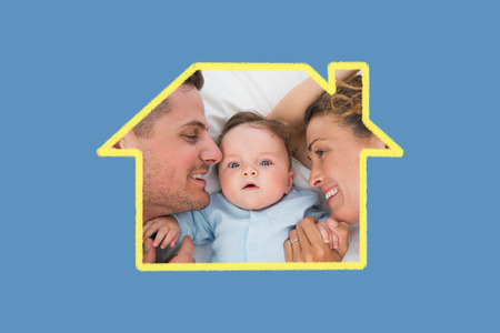 Cute baby with parents in bed against blue background with vignetteの写真素材