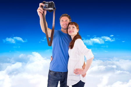 Couple using camera for picture against bright blue sky over cloudsの写真素材