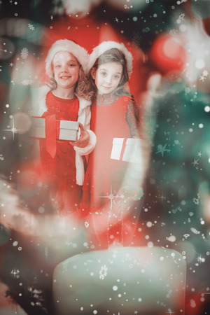 Festive little girls smiling at camera with gifts against candle burning against festive backgroundの写真素材