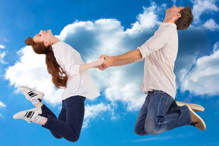 Couple jumping and holding hands against cloudy sky