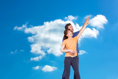 Happy couple pointing upwards together against cloudy skyの写真素材