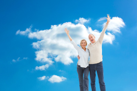 Happy mature couple cheering at camera against cloudy sky