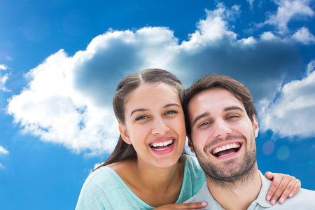 Cute couple smiling at camera against cloudy skyの写真素材