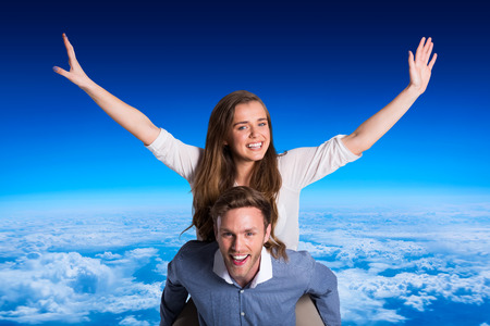 Smiling young man carrying woman against blue sky over clouds at high altitudeの写真素材