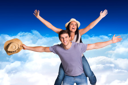 Man giving his pretty girlfriend a piggy back against bright blue sky over cloudsの写真素材