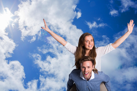Smiling young man carrying woman against bright blue sky with clouds