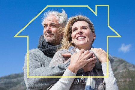 Carefree couple hugging in warm clothing against house outlineの写真素材