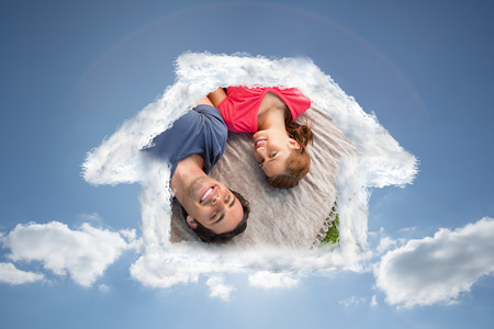 Two friends looking towards the sky while lying on a quilt against cloudy sky with sunshineの写真素材
