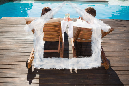 Couple toasting champagne by swimming pool against house outline in cloudsの写真素材