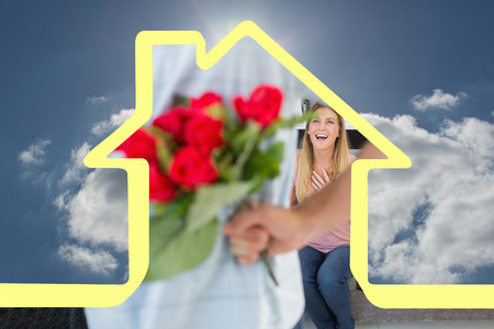 Man hiding bouquet of roses from smiling girlfriend on the couch against blue sky with clouds and sunの写真素材