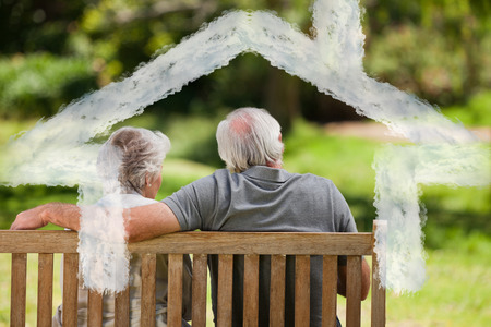 Couple sitting on the bench with their back to the camera against house outline in cloudsの写真素材