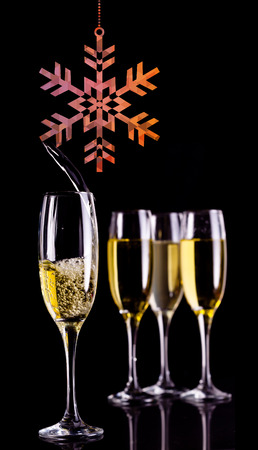 Hanging snowflake against full glasses of champagne and one being filledの写真素材