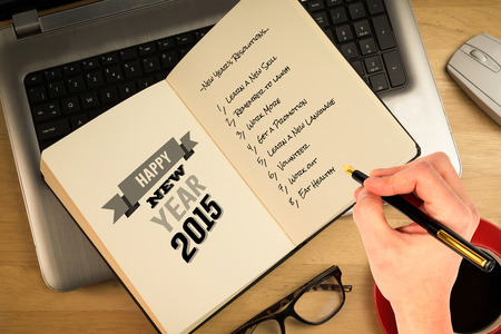 Hand holding a fountain pen against overhead of open notebook on laptopの写真素材