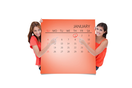 Teenage girls looking at the camera while pointing their fingers on a blank poster against orange cardの写真素材