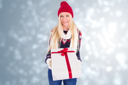 Festive blonde holding a gift against light design shimmering on silverの写真素材