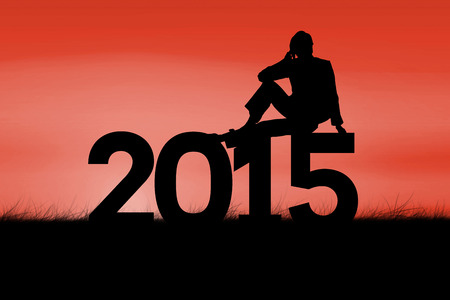 Silhouette of woman sitting against red sky over grassの写真素材