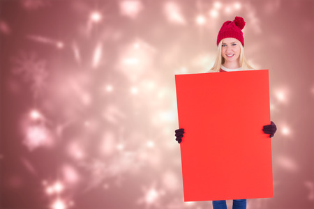 Festive blonde showing a red poster against snowflake design shimmering on redの写真素材