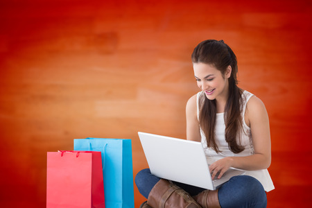Smiling brunette sitting and using her laptop against blurred wooden planksの写真素材