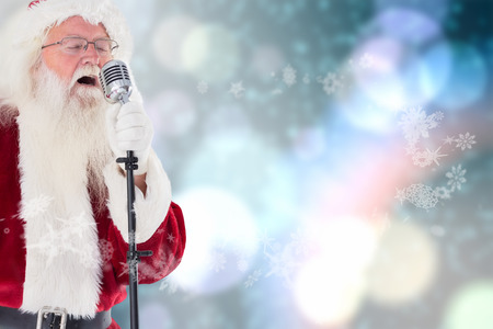 Santa Claus is singing Christmas songs against light glowing dots on blueの写真素材