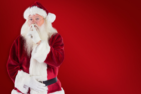 Santa asking for quiet to camera against red backgroundの写真素材