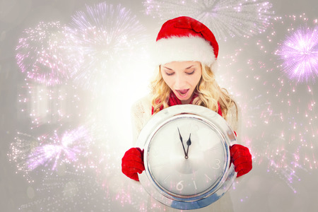 Festive blonde holding large clock against colourful fireworks exploding on black background