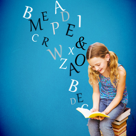 Cute little girl reading book in library against blue backgroundの写真素材